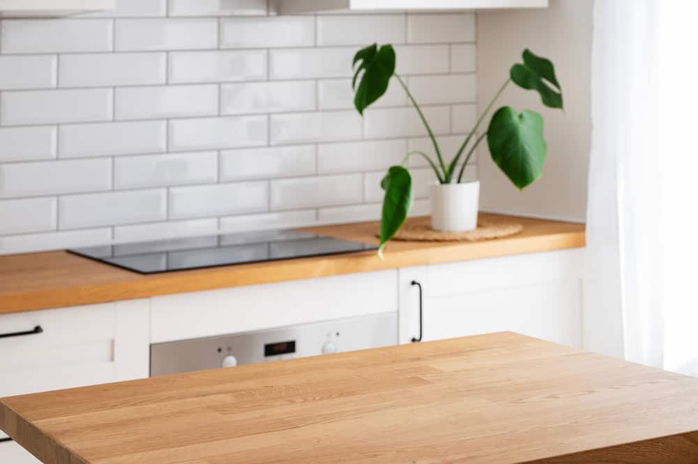 A modern kitchen with a wooden countertop and white cabinets showcases the quality of expert craftsmanship you'd expect from top-notch reconstruction services. A green potted plant sits on the counter, while white subway tiles embellish the backsplash. Bright, natural light fills the space.